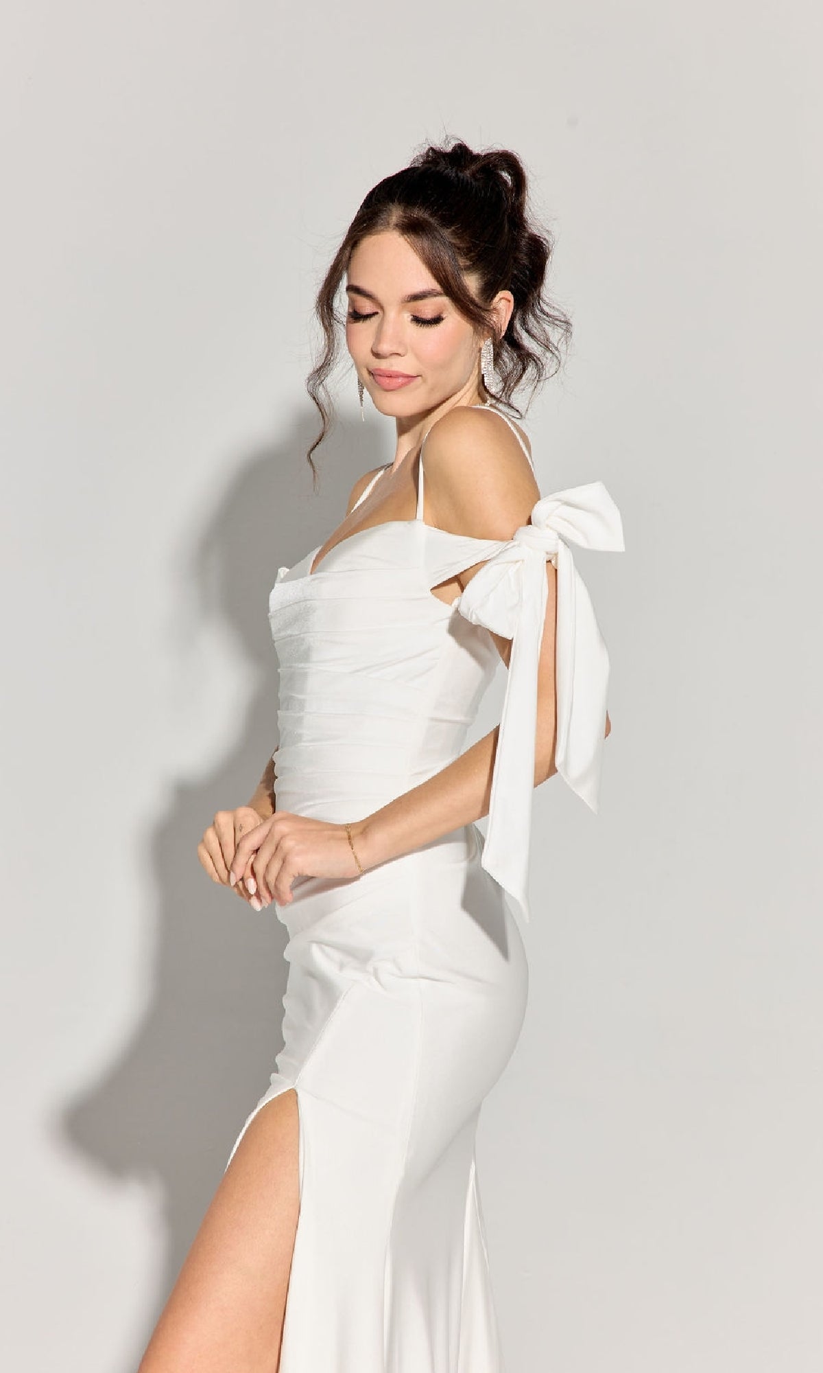 Woman in the Eureka 9181 Shoulder-Ties Long Jersey Prom Dress, featuring a white silky finish, formal style, shoulder bow, and thigh-high slit, standing against a plain light background.